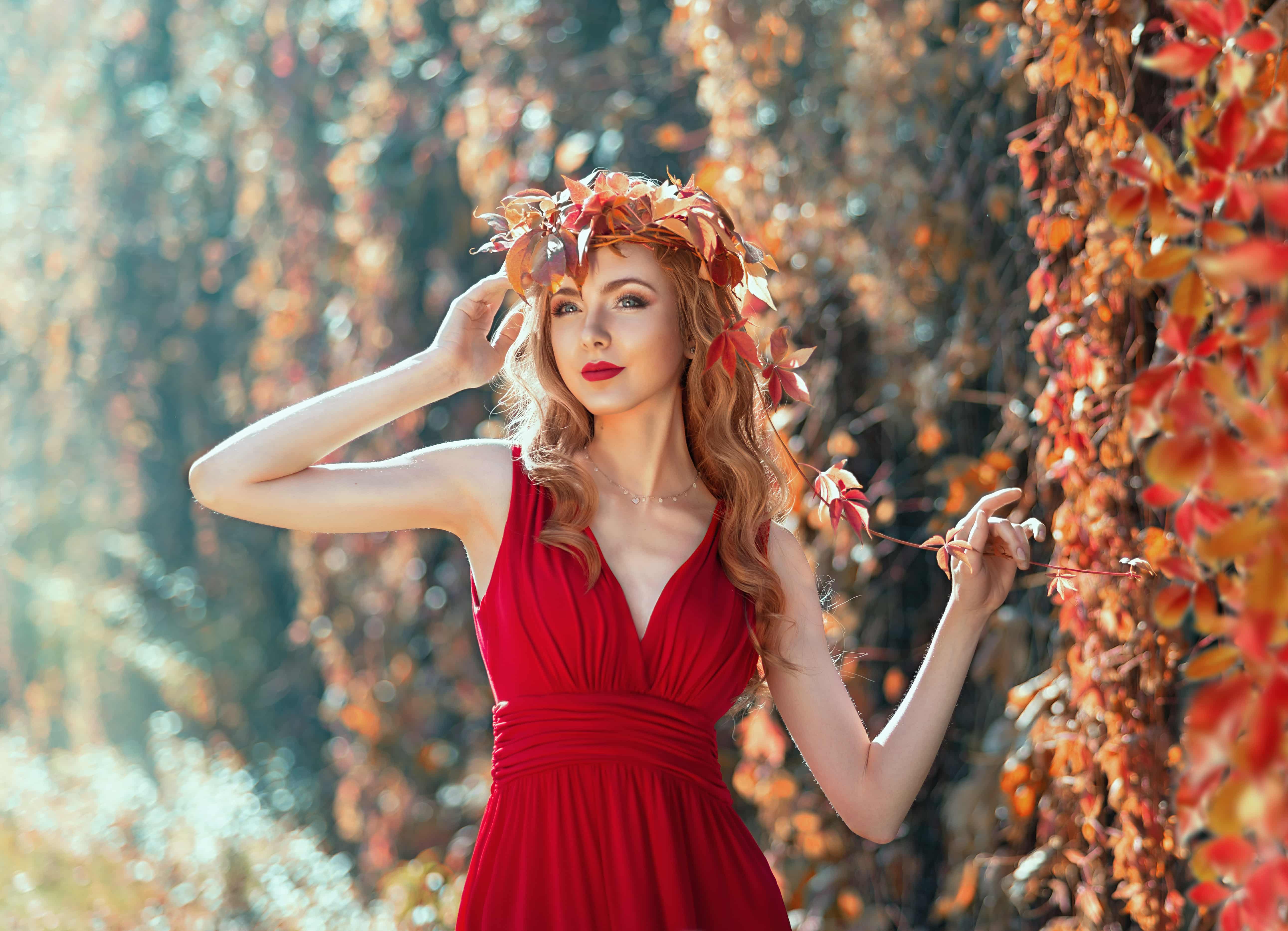 woman with curly red hair in a red dress a head wreath of flowers outdoor