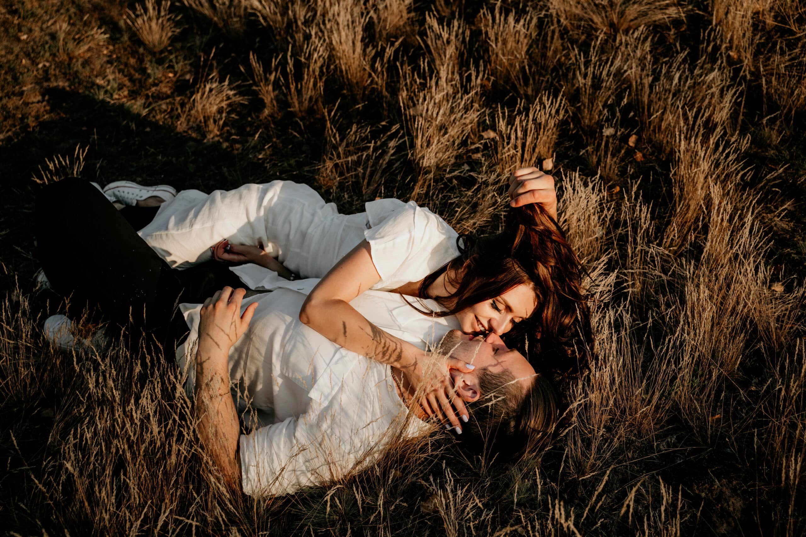 Loving couple laying and kissing on the grass at sunset in summer. 