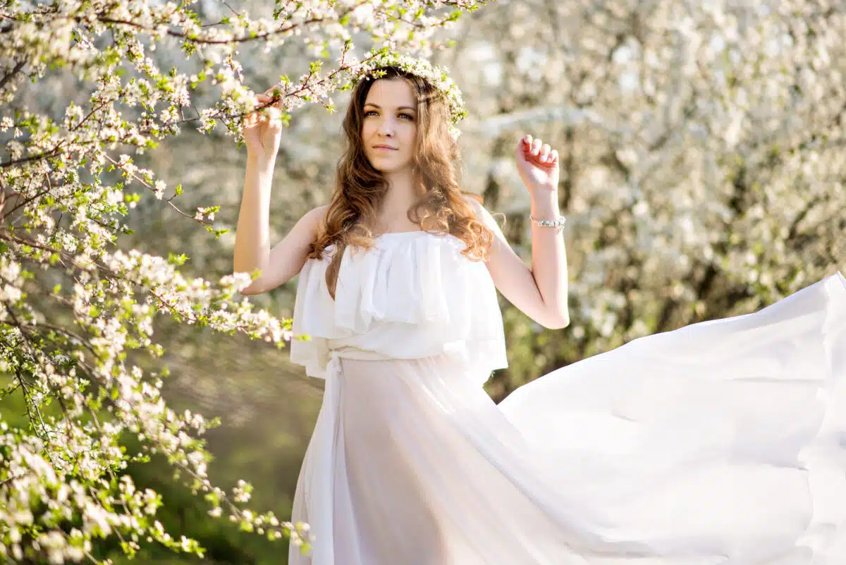 Beautiful young woman in white dress and head wreath of flowers