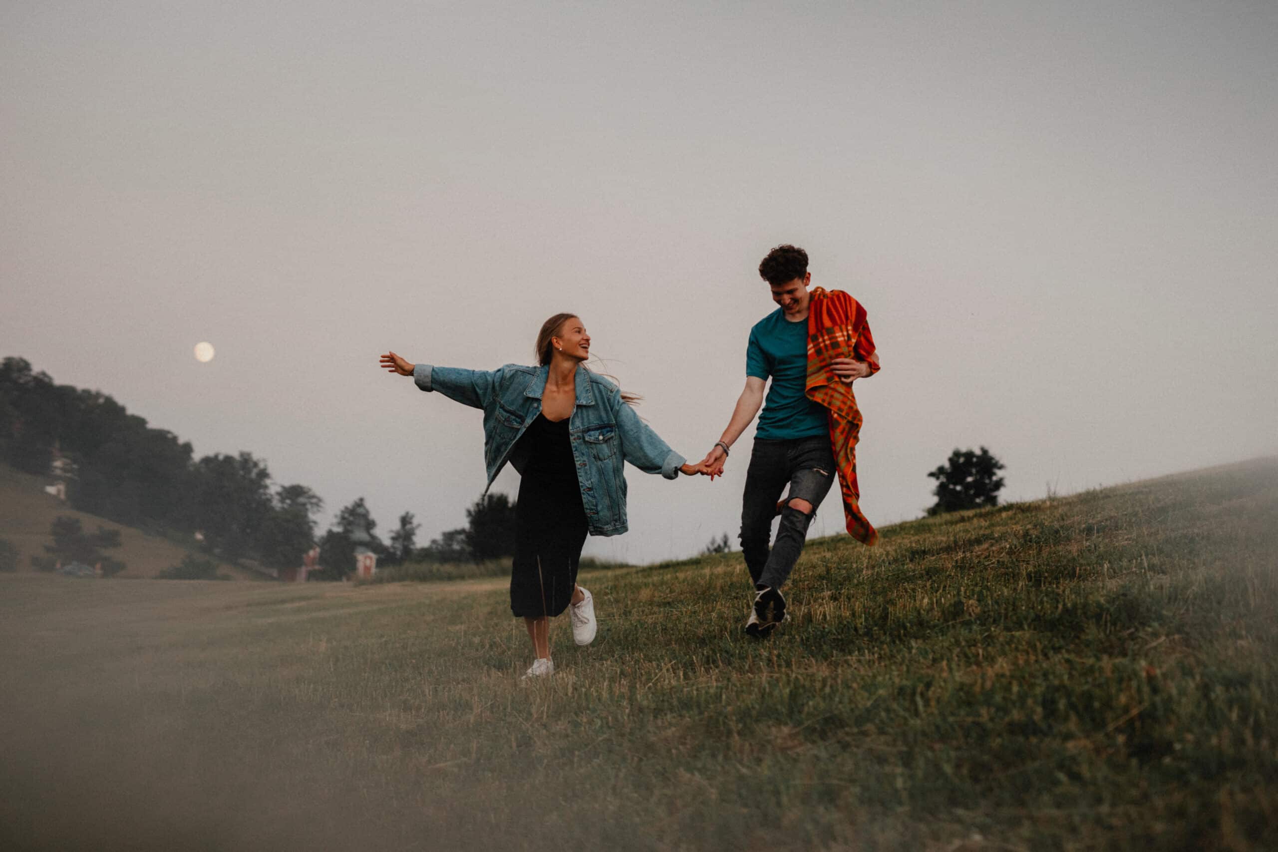 Young couple walking in nature at sunset in countryside, holding hands and running.