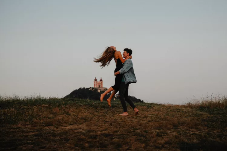 Young couple on a walk in nature at dusk in countryside, having fun hugging