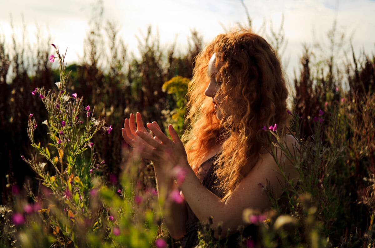 Woman with beautiful cascading long red hair standing amongst wild flowers