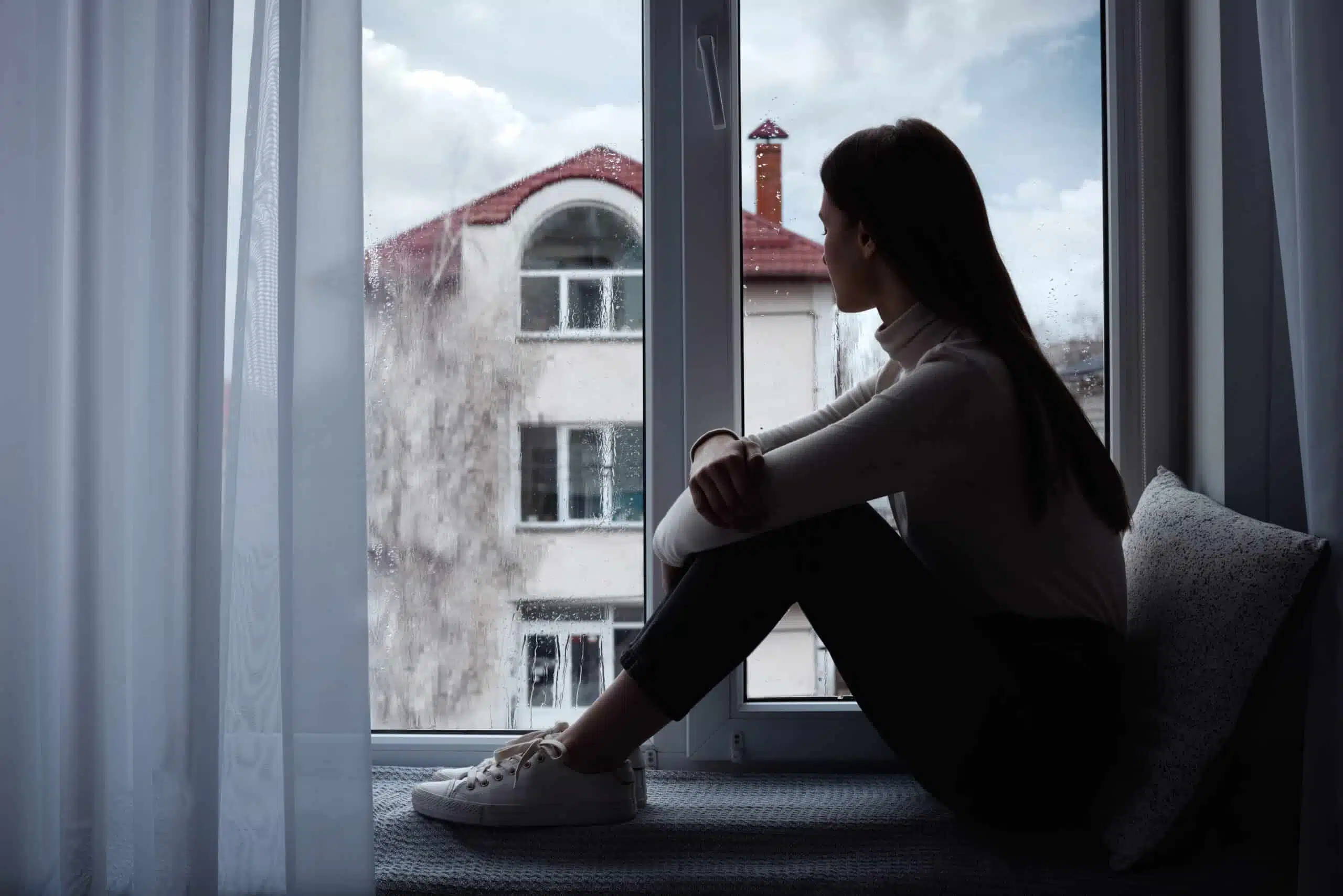 Melancholic young woman looking out of window indoors