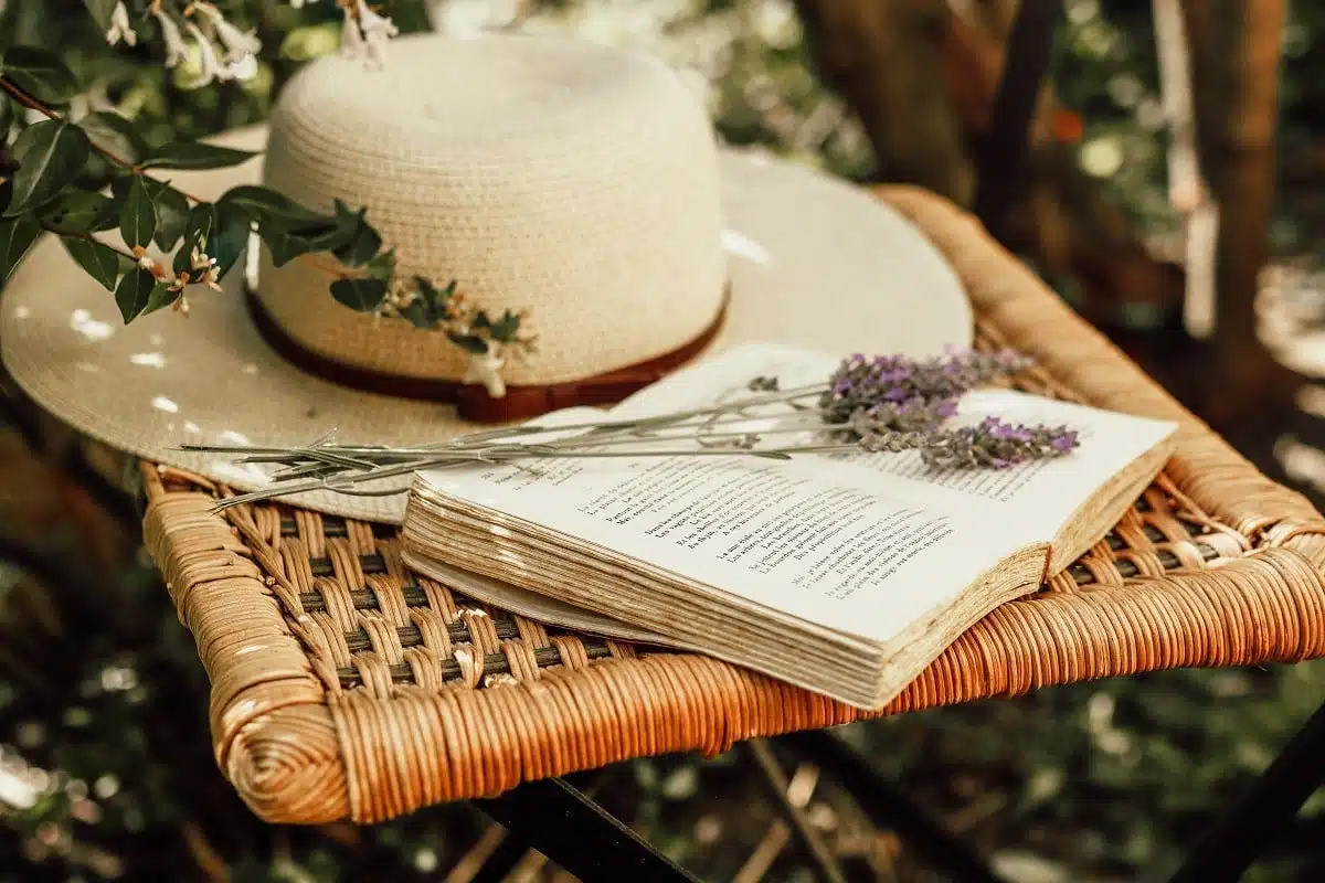 Lavender bouquet on open book and woman's summer hat on old wicker chair in the garden.