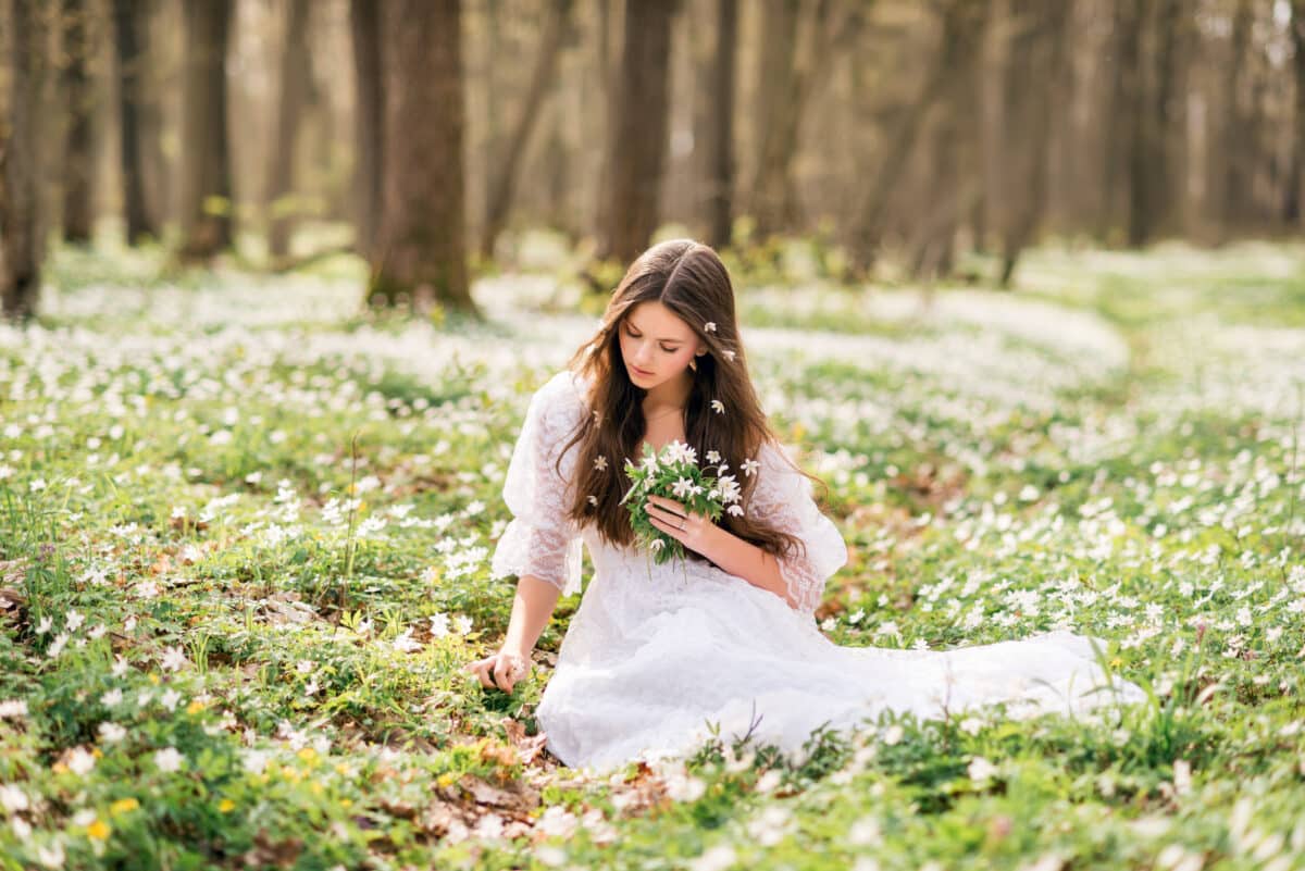 young beautiful nymph in a white dress collects primroses in the woods