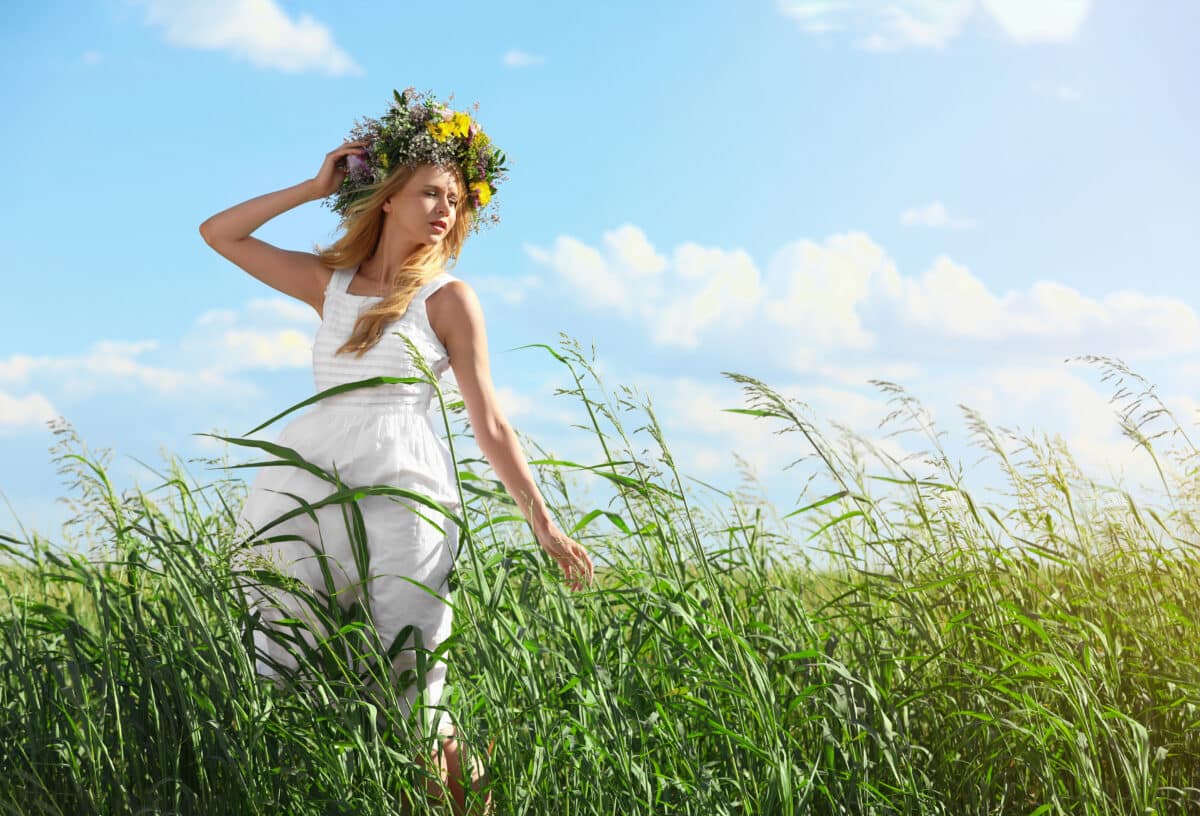 a young woman wearing a wreath made of beautiful flowers in the field of grass