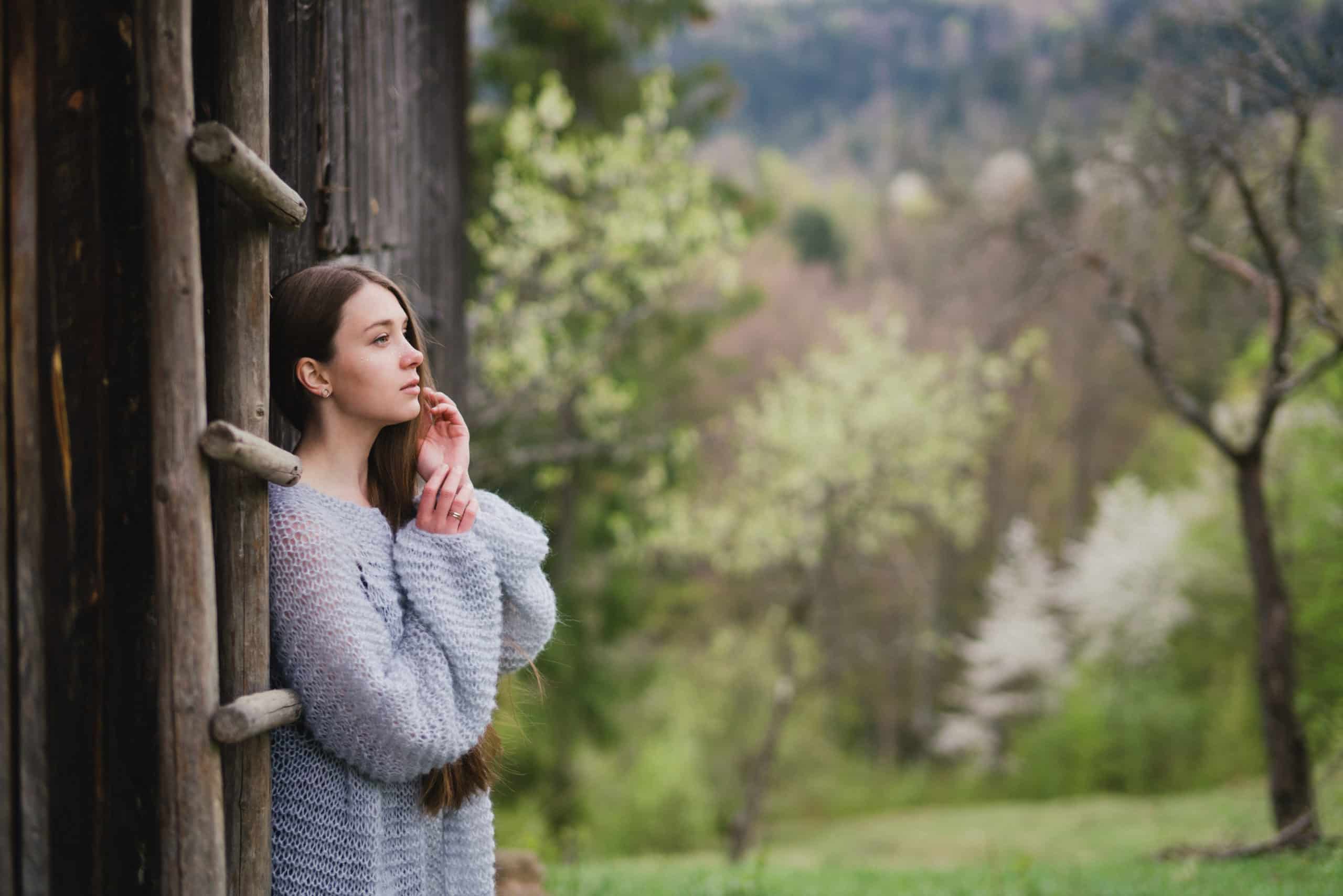 Young woman in grey sweater emotional standing by the cottage.