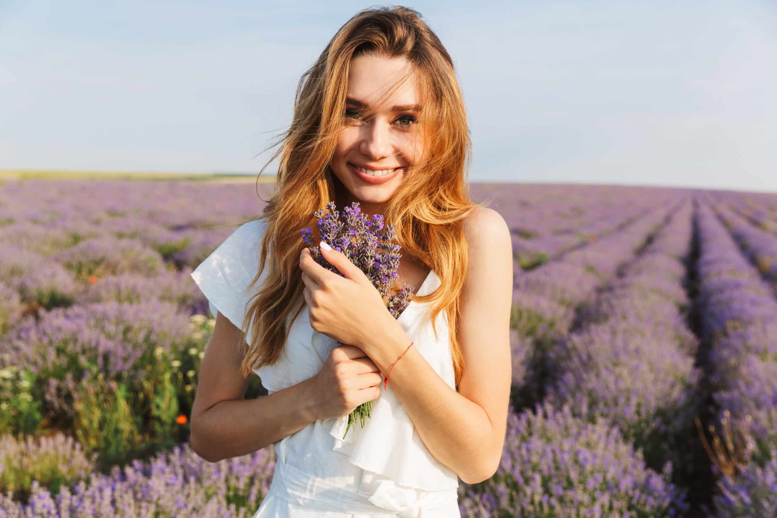 Happy young woman in dress holding bouquet with flowers in lavender field.