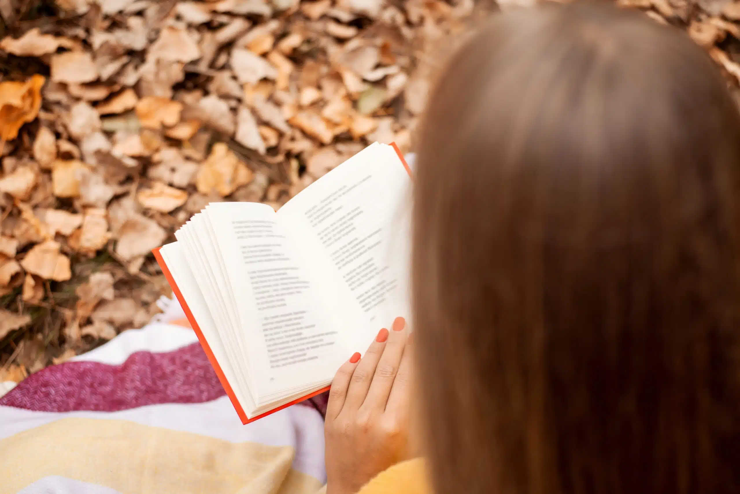 Young woman reading some poems in colorful autumn park, sitting on the leaves and grass.