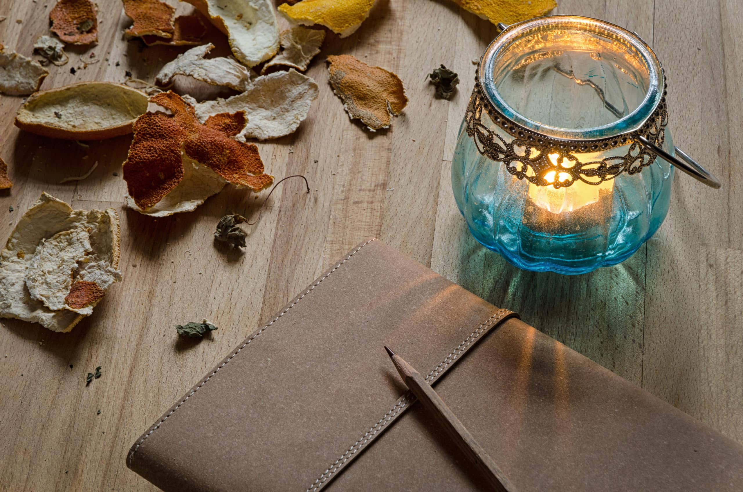 Vintage notebook, pencil, and candle lantern with dried leaves on wooden table.