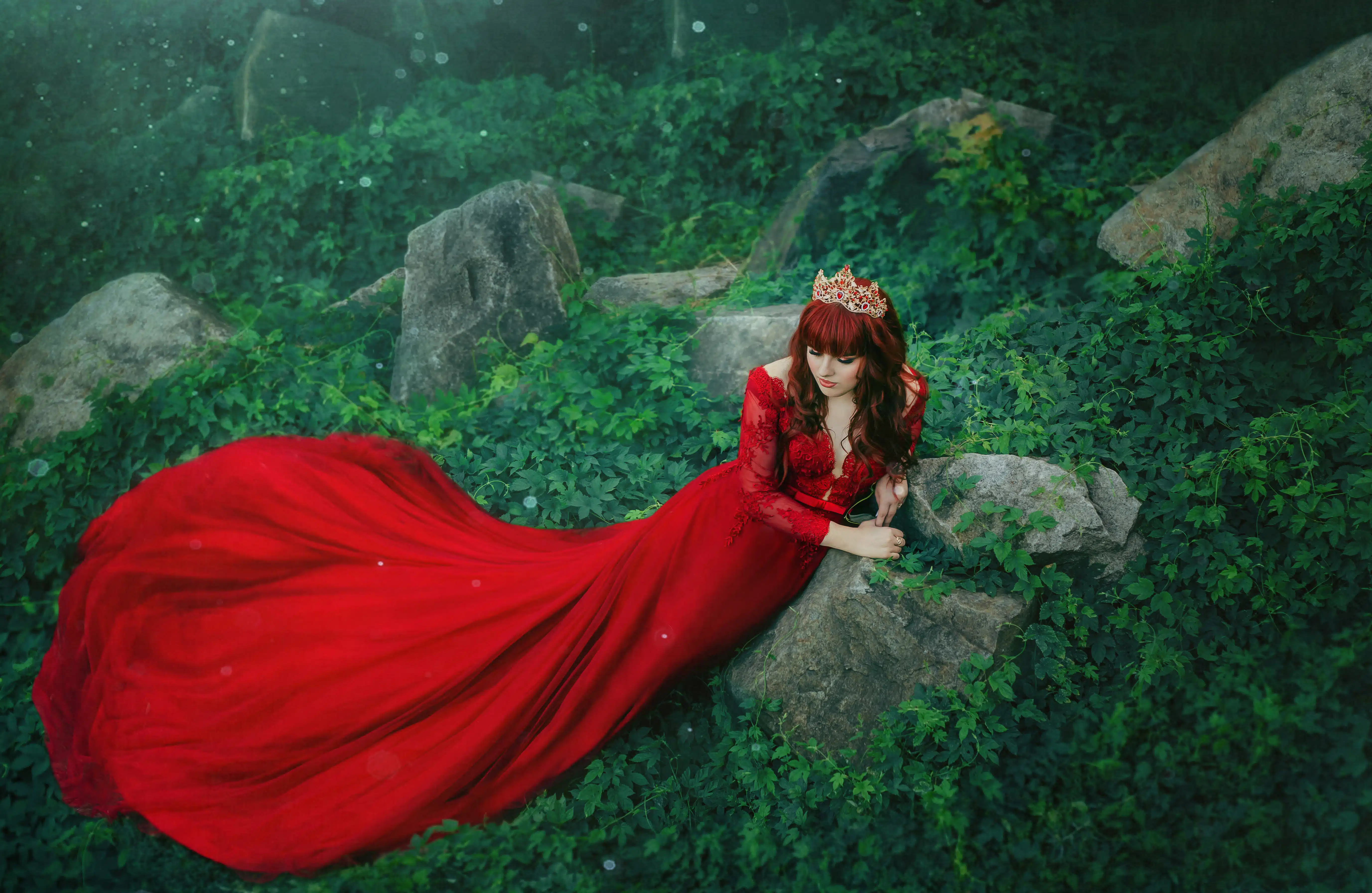 The Queen in a luxurious, expensive, red dress, with a long train lies on the thickets of ivy.