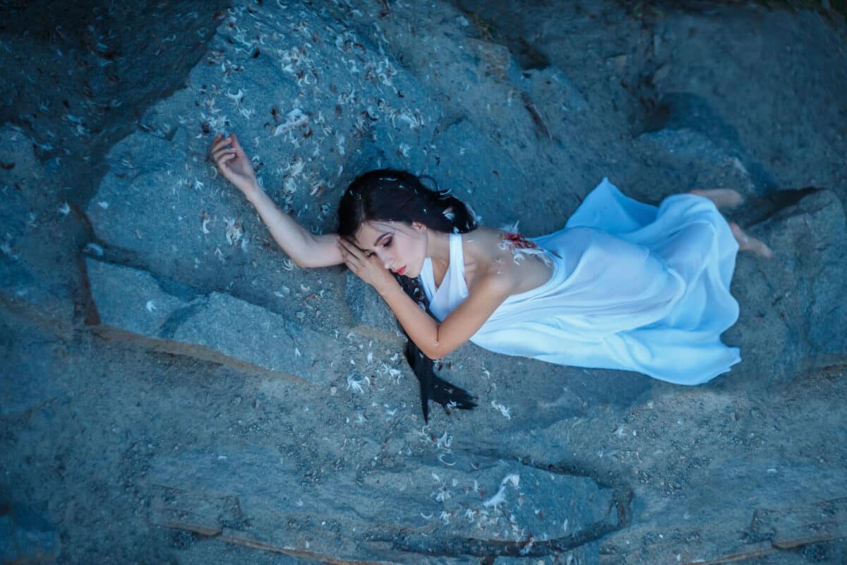 a beautiful fallen angel in white dress lying on the rocks