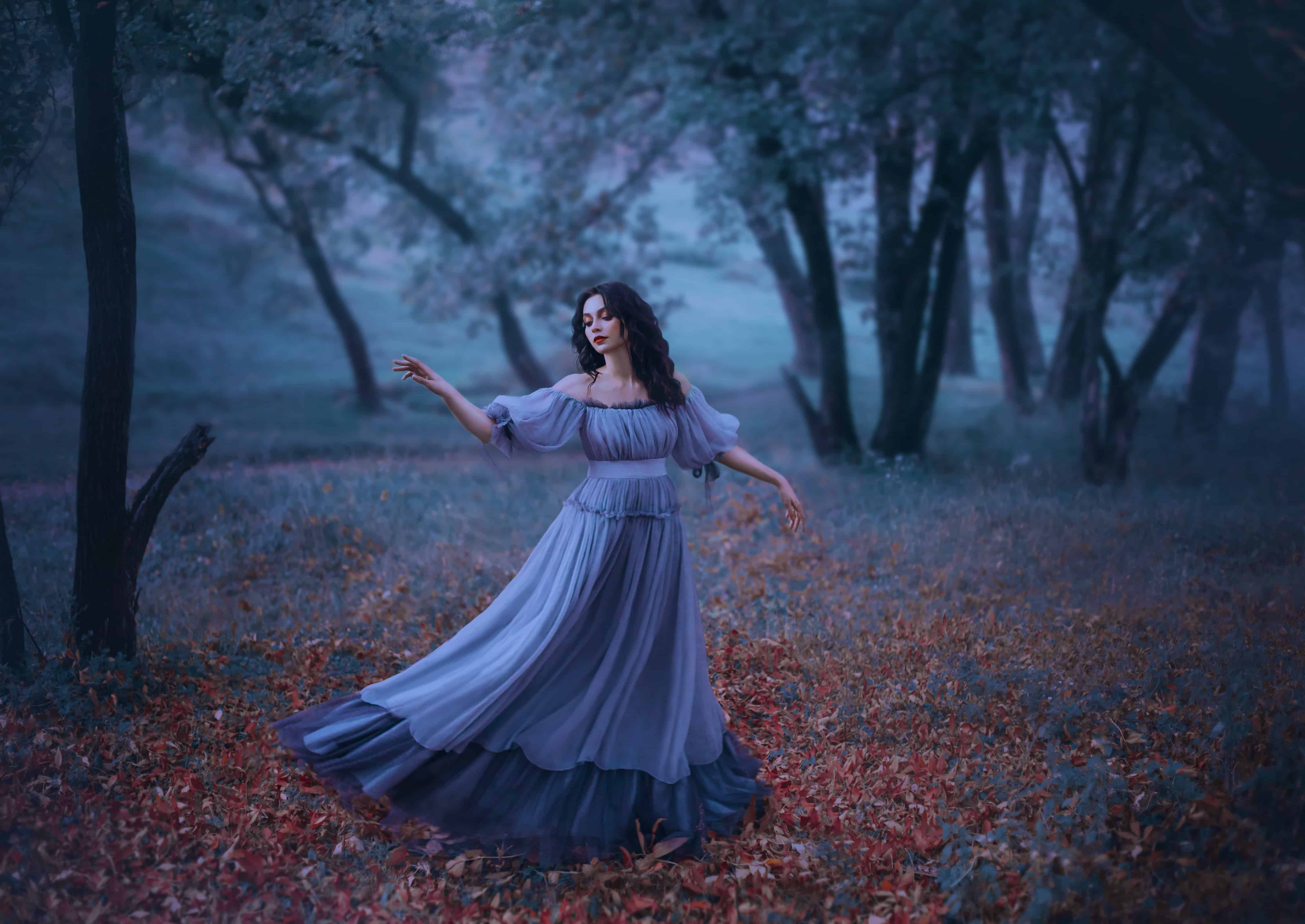 a mysterious girl with wavy dark hair is dancing alone on fallen autumn leaves in a gloomy night forest in a long wonderful blue vintage dress, fabulous heroine, knows no ills, the legend of Pandora