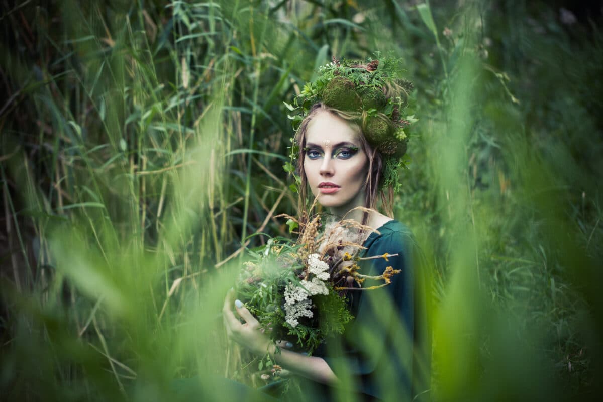 Beautiful fairy among the tall grasses in the forest holding some wild flowers