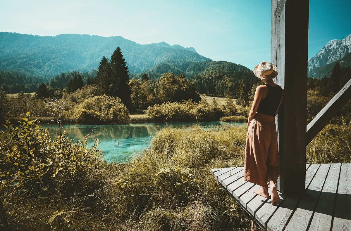 Woman looking toward the lake and the forest, enjoying freedom on nature outdoors.