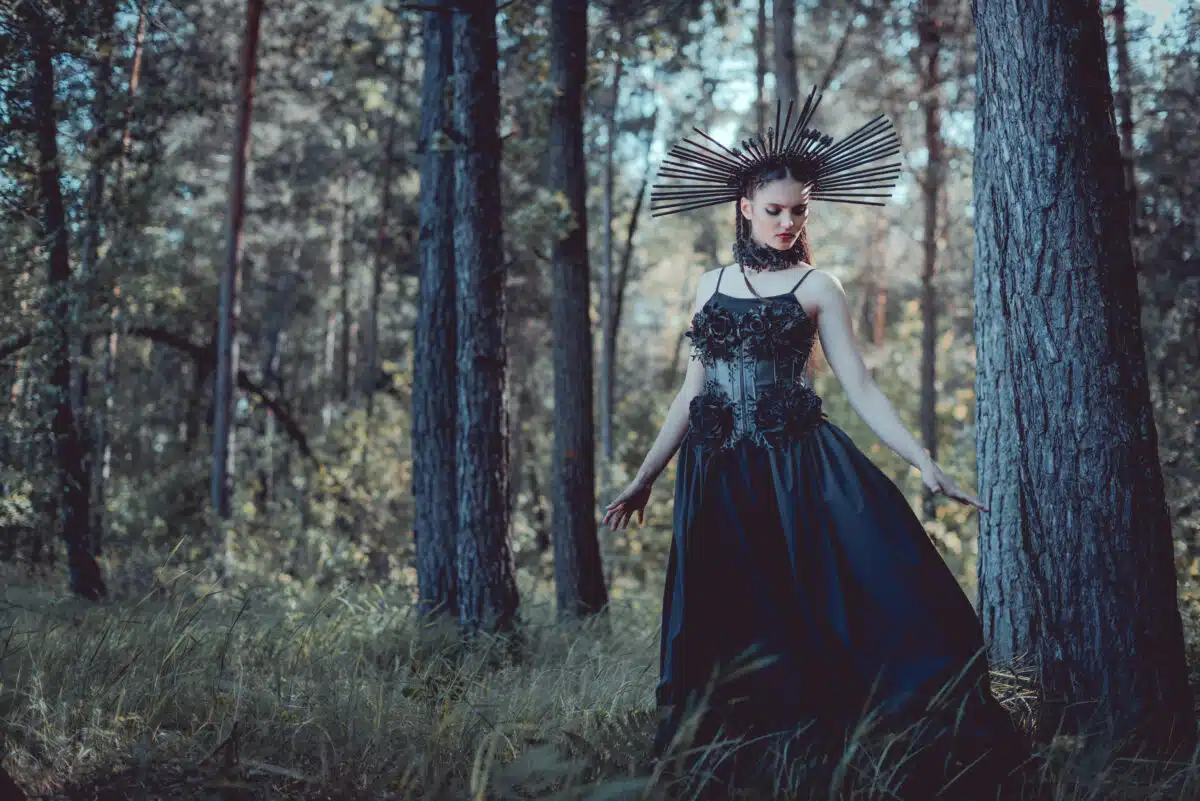 beautiful woman in witch costume walking on forest, looking away