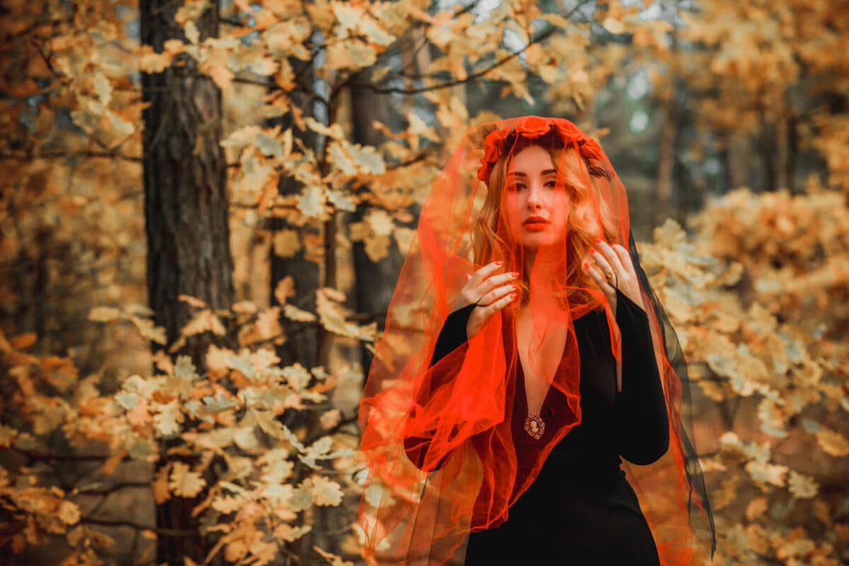 mysterious lady in black dress her face covered in a red veil standing in the forest 