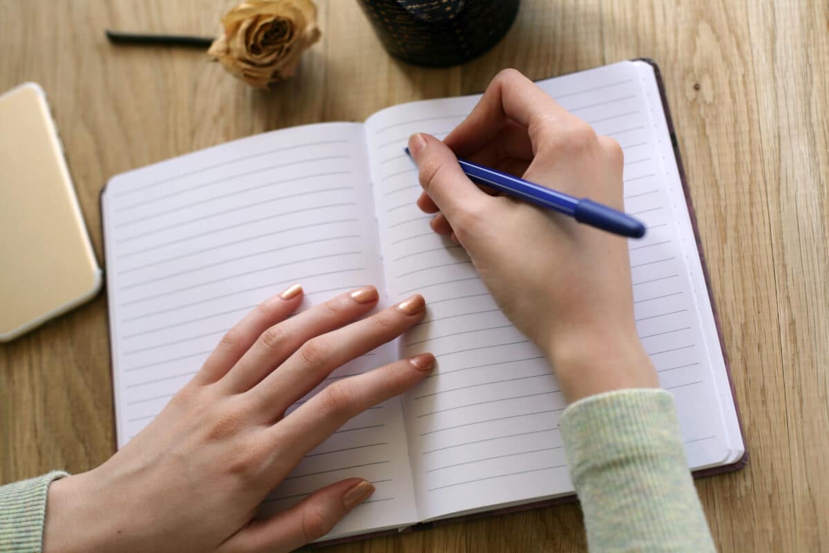 Top view of woman hands writing on open notebook .