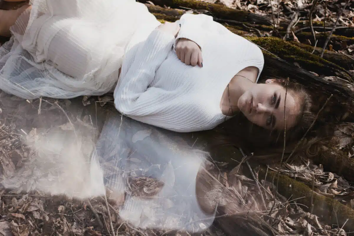 young woman in white dress is lying on the ground with her reflection