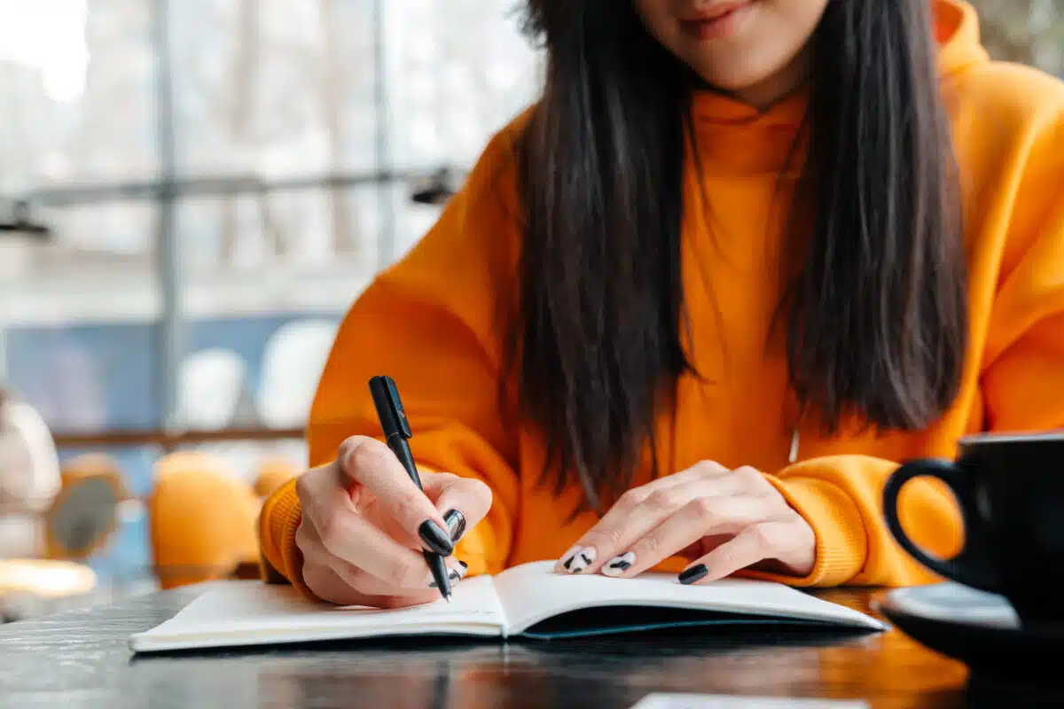 Pleased asian woman writing down notes while sitting in cafe