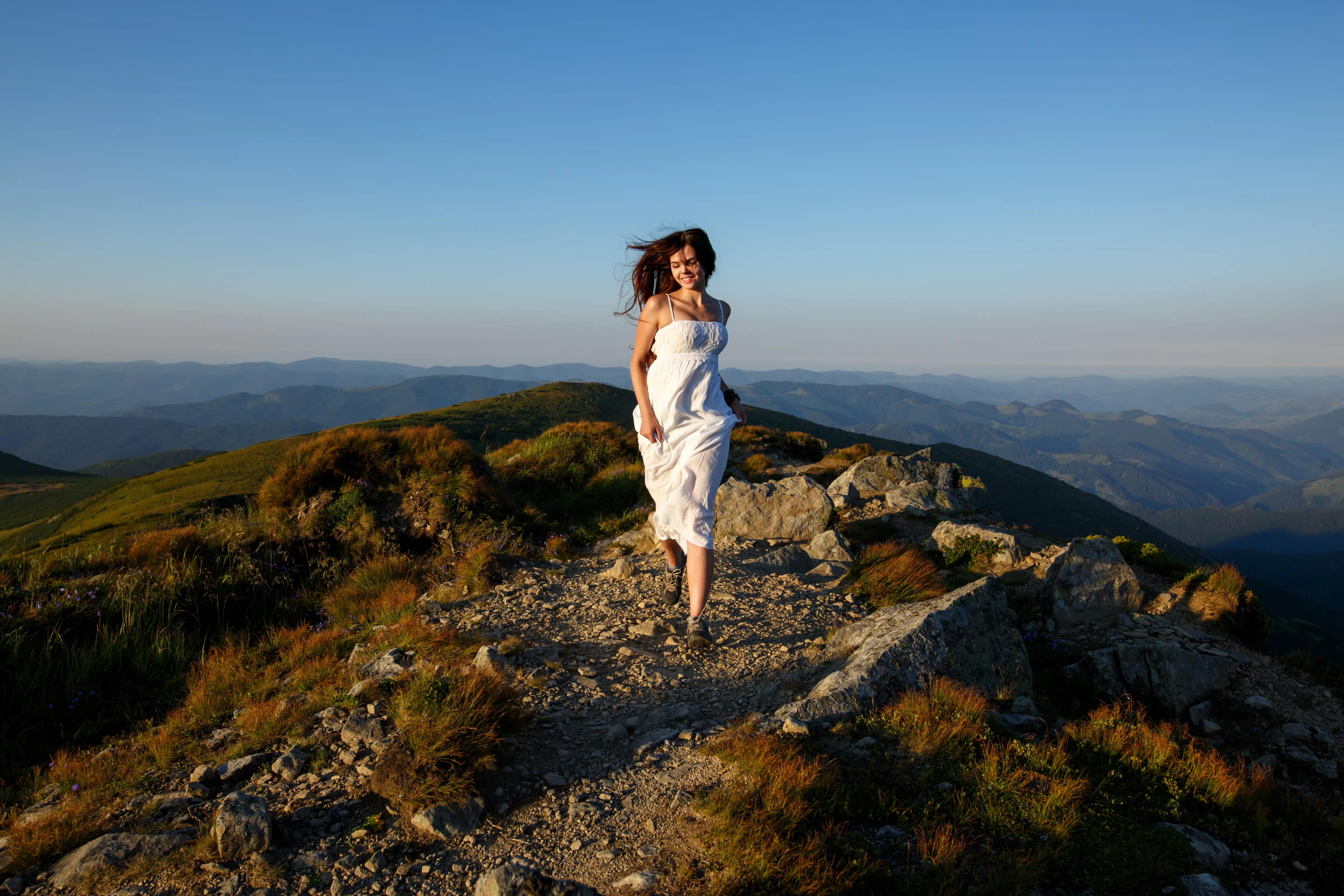 Beautiful woman in a long white dress running in the mountains