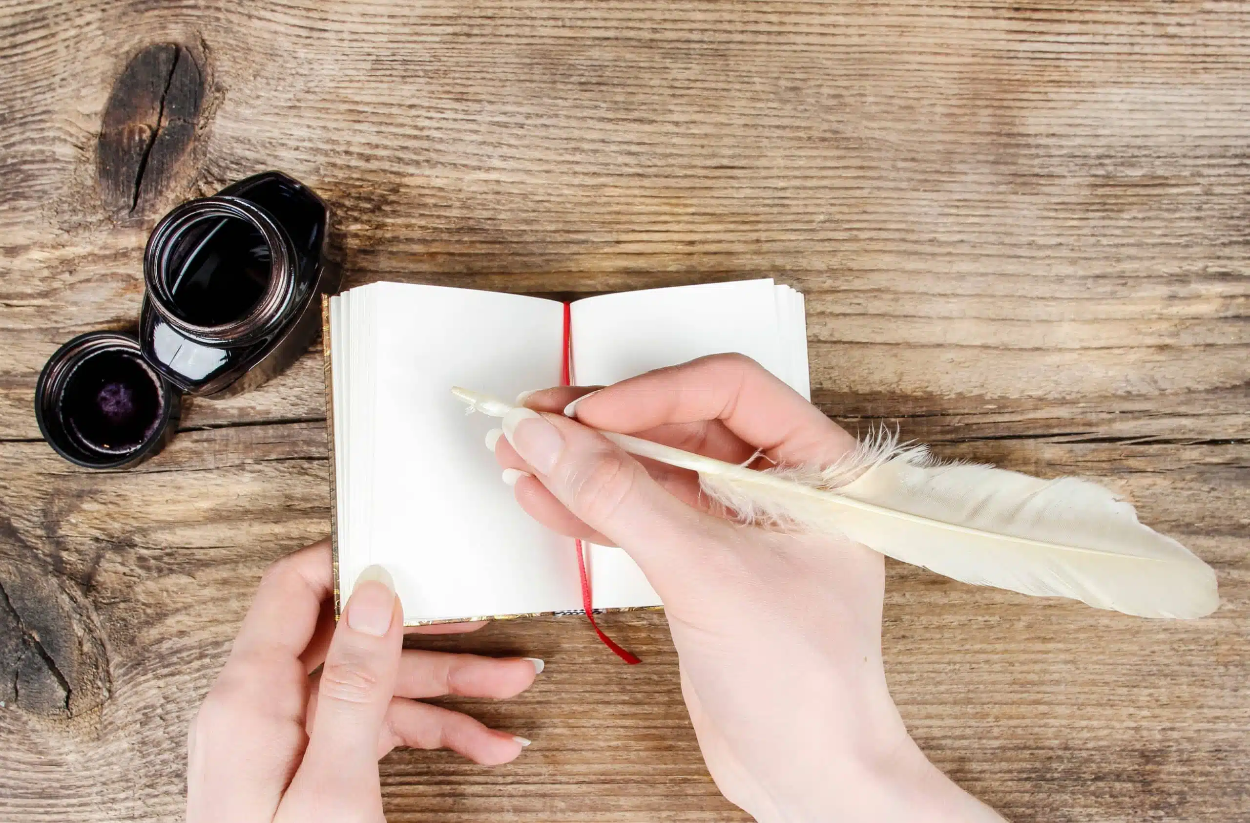 Woman writing on notebook with white quill pen.