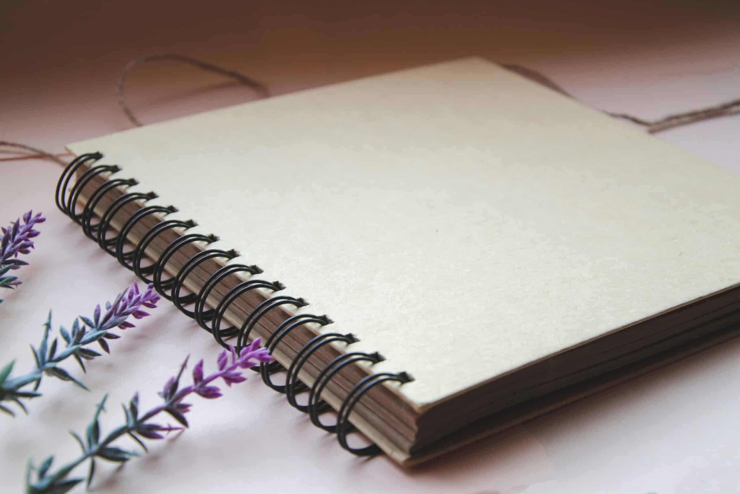 Brown spiral notebook on light background with lavender flowers