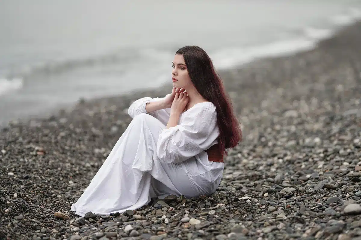 lady in a white dress on a pebble beach near the gray sea