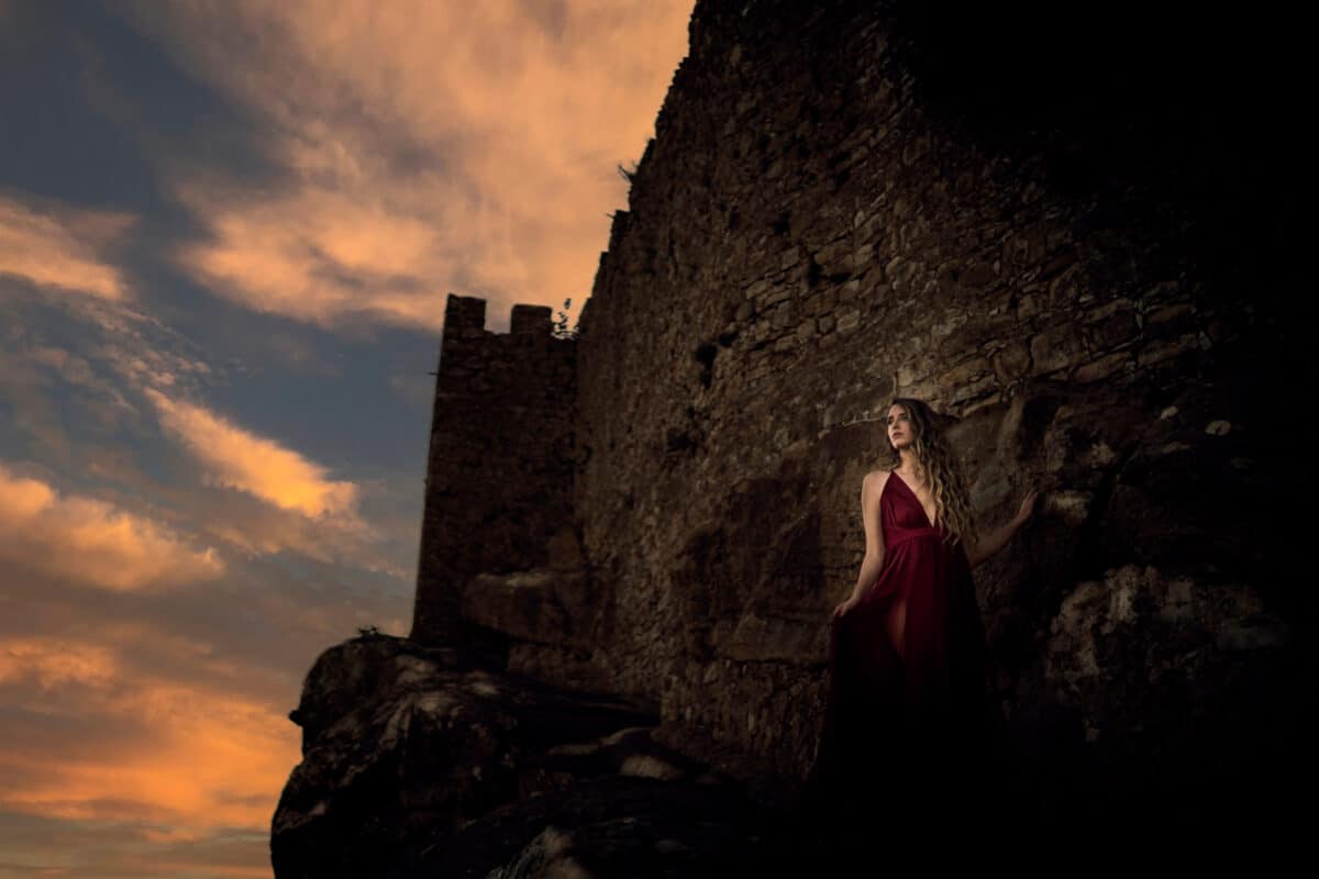 Chica joven con vestido rojo en zona boscosa y castillo medieval