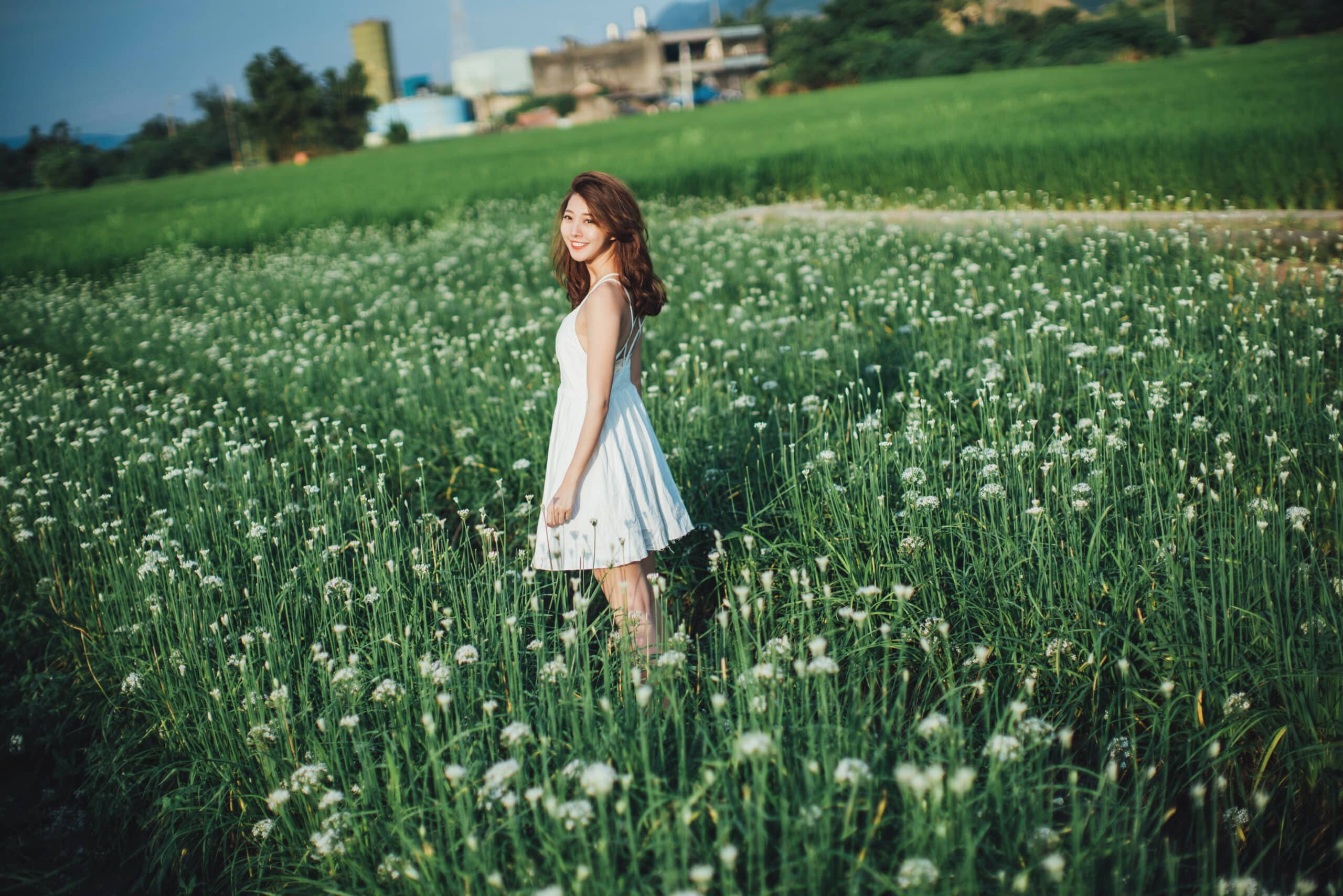 cute asian girl standing in the middle of a field of flowers.