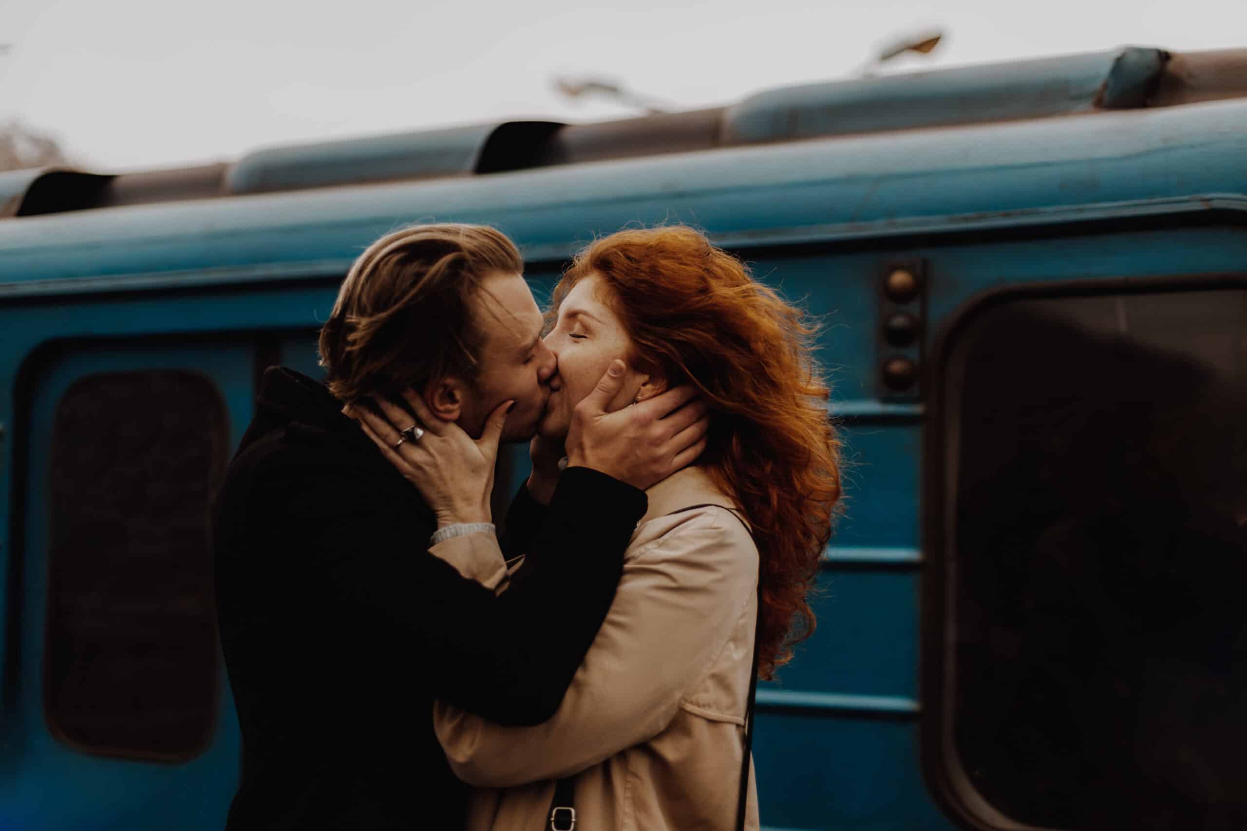 Young couple in love kissing against train in train station.