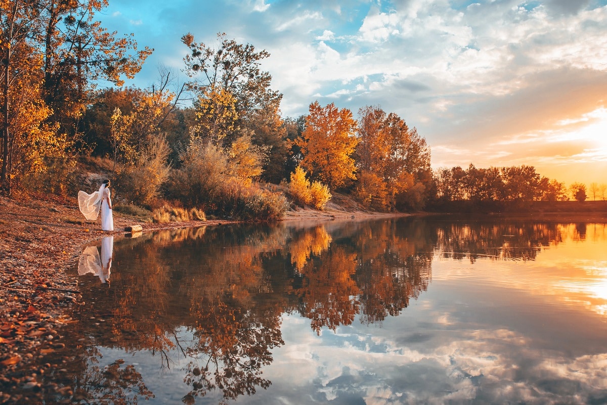 lady in white dress standing by the lake in autumn evening