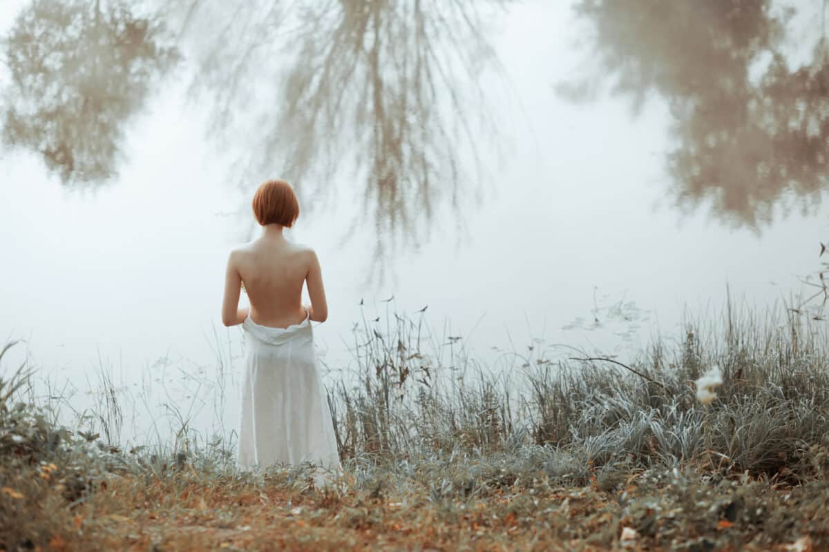 Half-naked woman standing in front of the misty lake