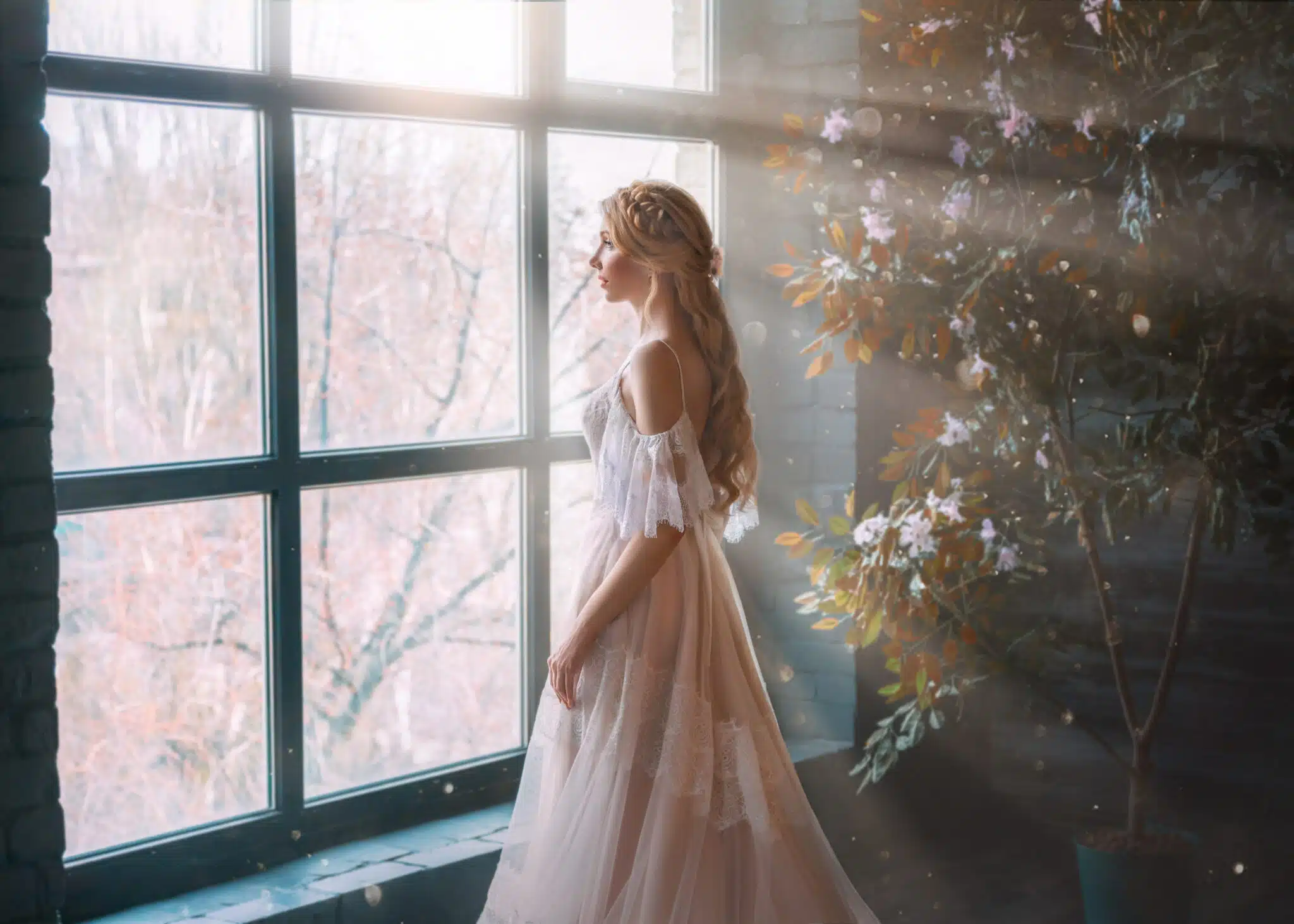 Romantic lady, blonde woman with long hair in white vintage dress stands in dark room, looks out window. 