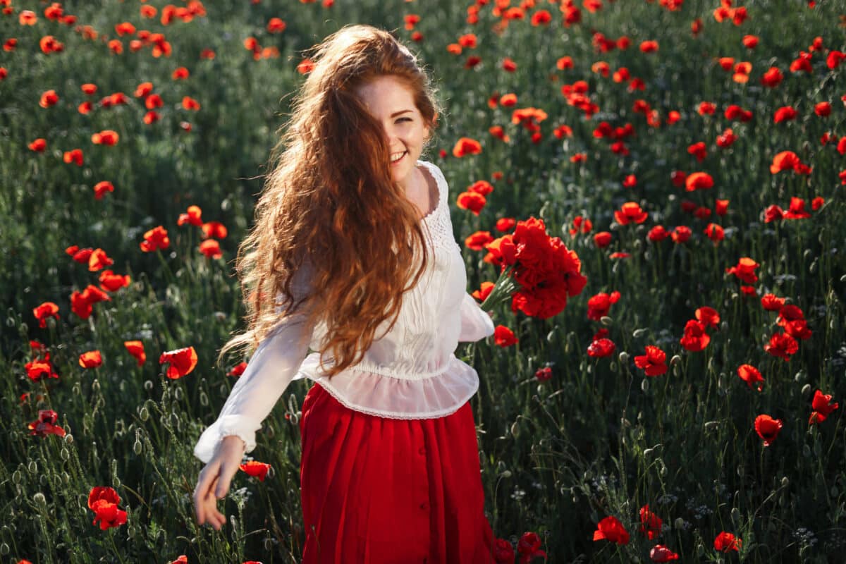 Young beautiful red head walking and dancing through a poppy field at sunset