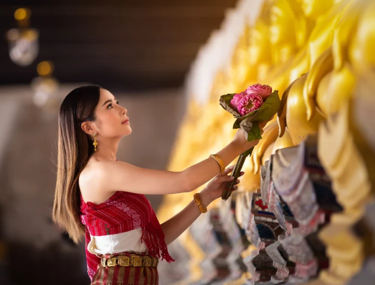Beautiful Thai woman offering a bouquet of lotus flowers to the golden Buddha.