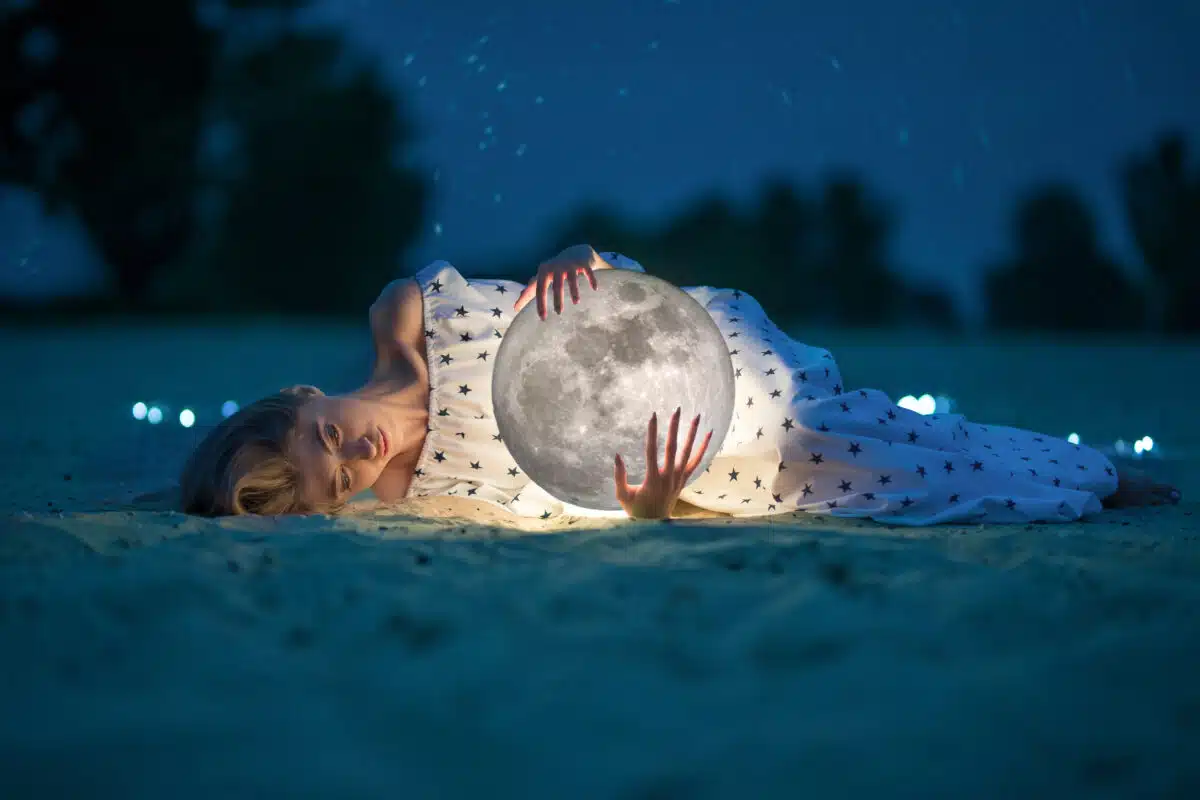 Beautiful lady on a night beach with sand and stars hugging the moon