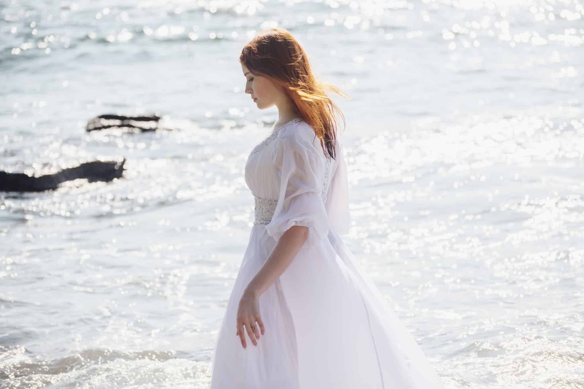 lonely young redhead woman walks on the beach in summer.