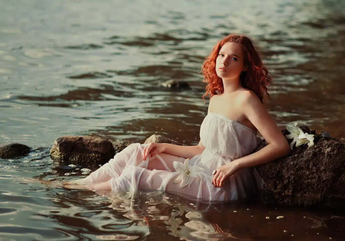 enchanting woman with flaming red hair sitting in the murky waters