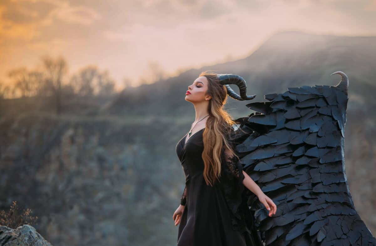 Fantasy lady in a black dress with huge wings. Demon with horns. Dark gothic fashion glamorous character woman. beauty queen. fabulous landscape of autumnal nature. Sunset with fog over the mountains