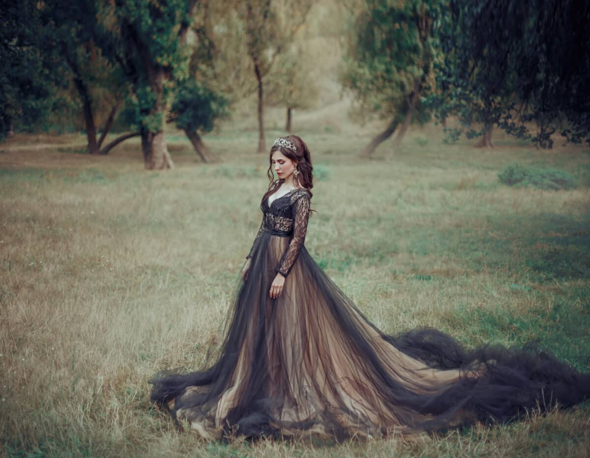 sad lady in a black dress and crown walking in the woods