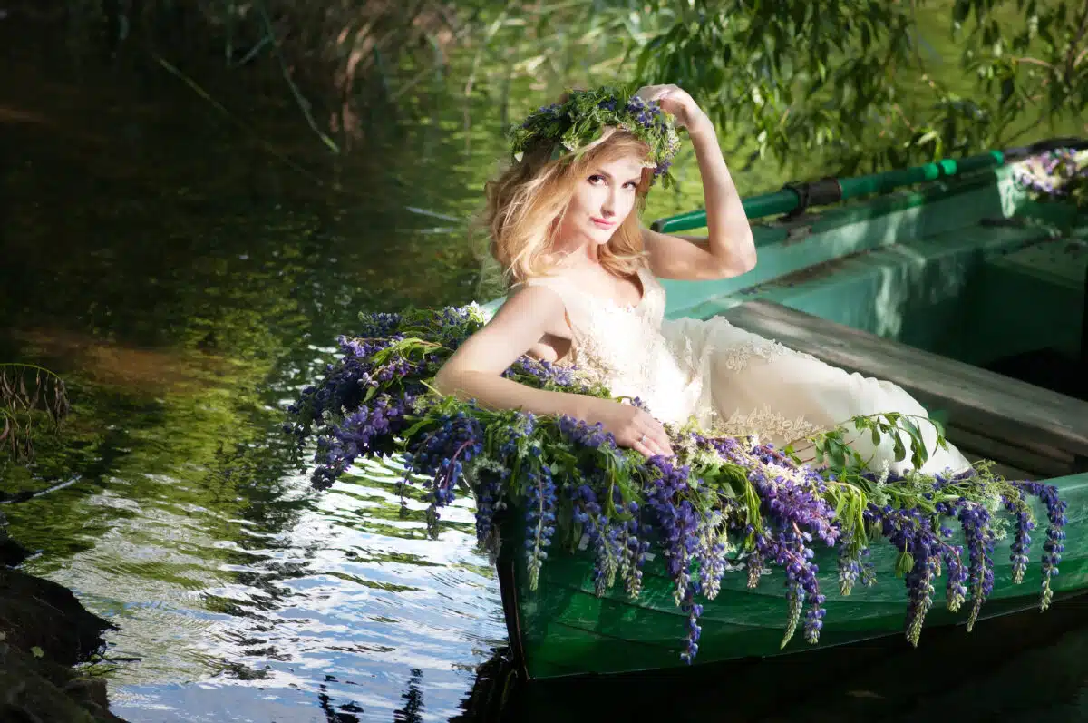 woman with wreath on her head sitting in a boat with flowers