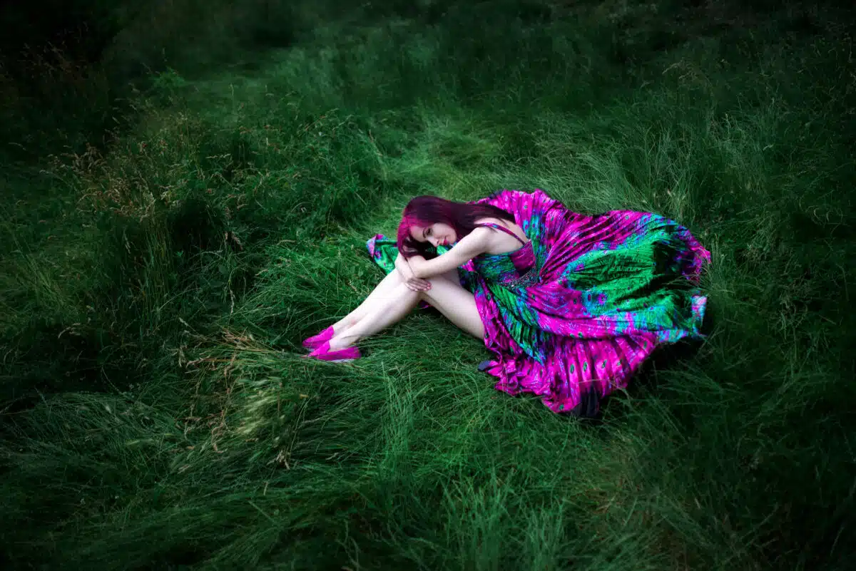 beautiful girl sits alone on the grass, bright dress, sadness