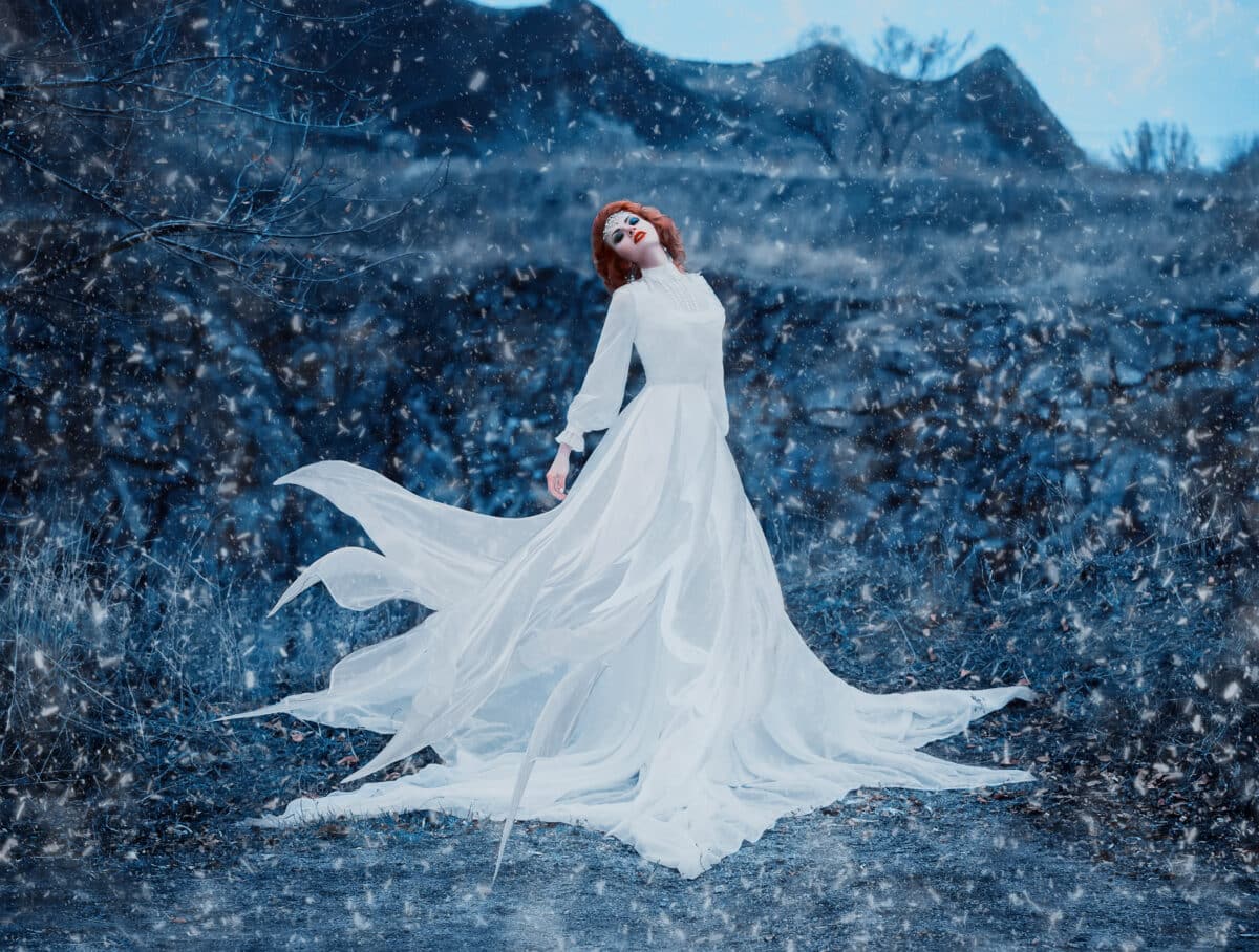 Luxury snow queen stands on top of the snow-covered mountains and looks into the distance,fashionable toning,creative computer colors