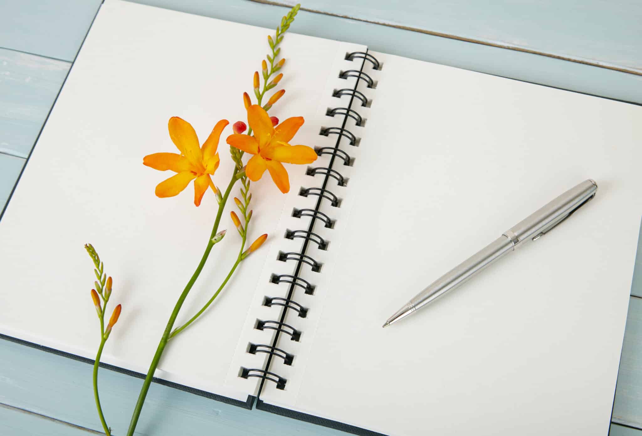 A blank journal with flowers on a painted wooden desktop
