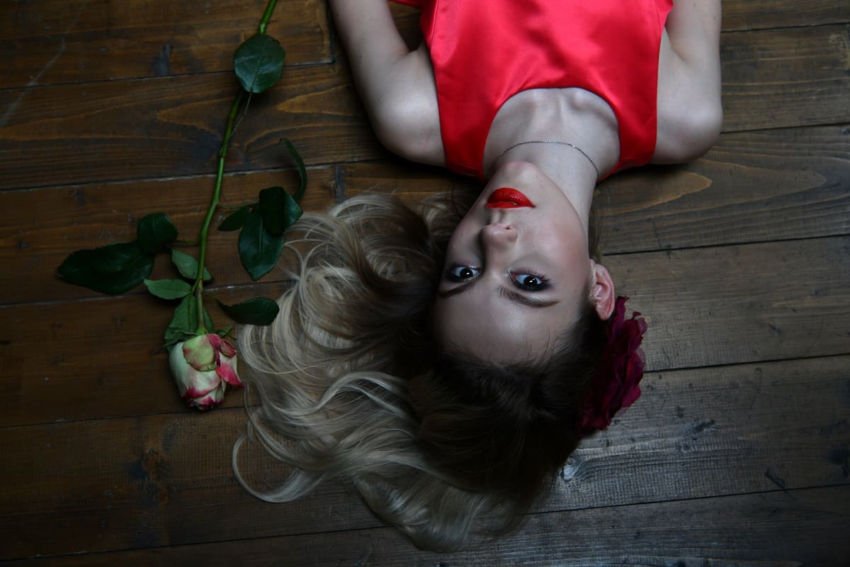 beautiful lady in an evening red dress lies on the floor in a dark room