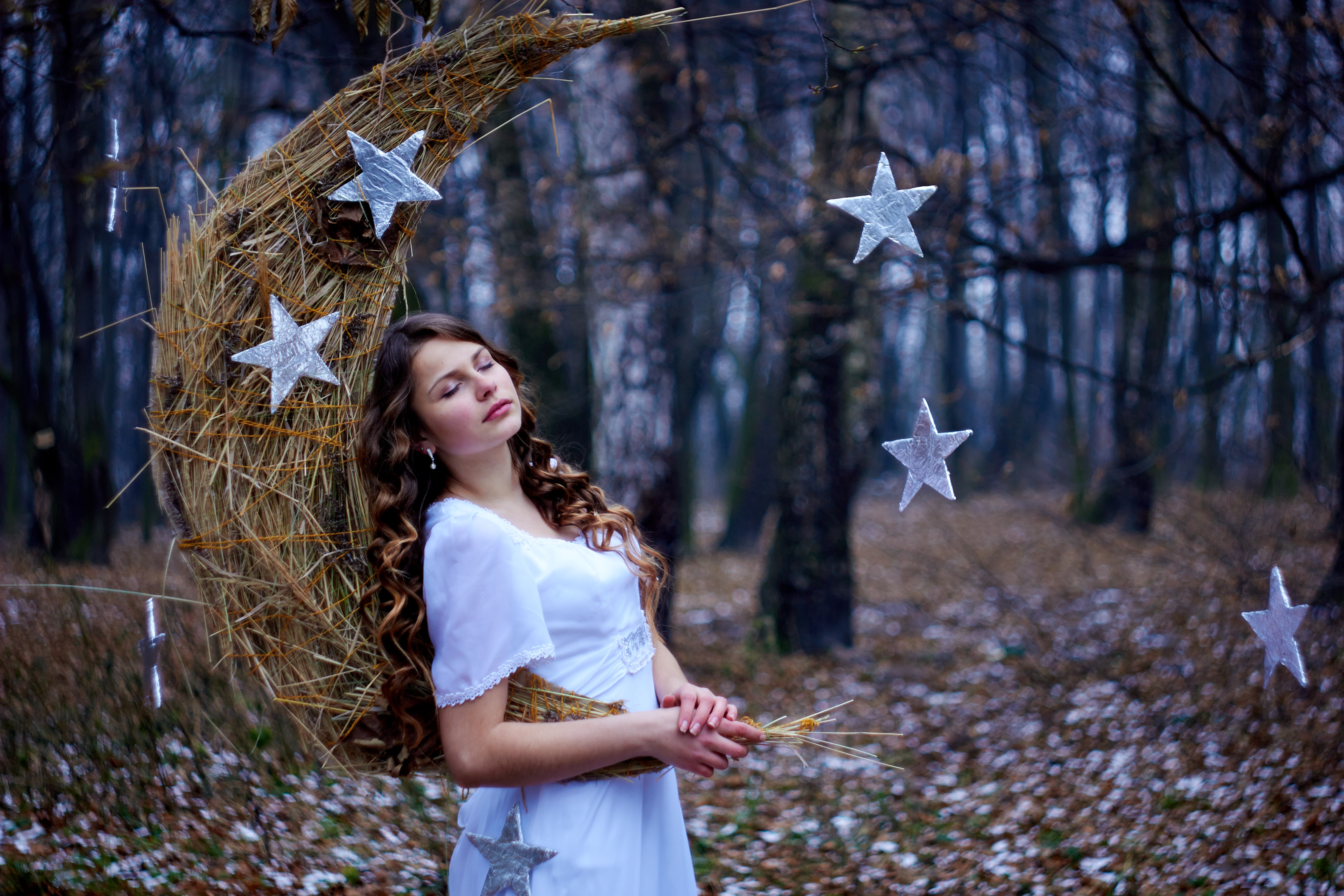 Beautiful young girl with brown curly hair. White dress on the perfect figure of the model. Month, handmade stars made of straw, cardboard, foil. New Year fairy tale, magic motive in the winter forest.