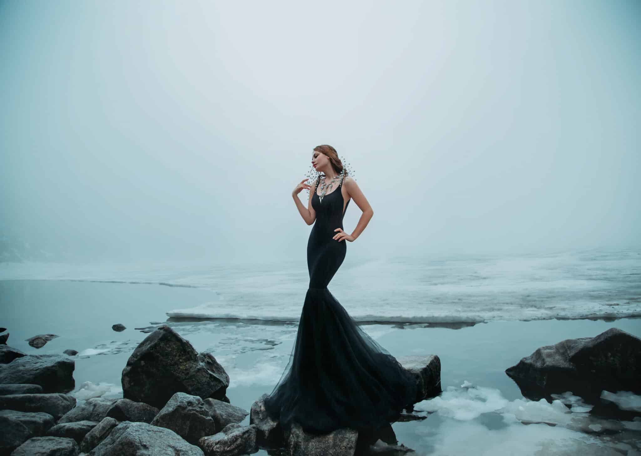 Sexy Woman long black dress silhouette mermaid tail fish. background river ice water stones cold snow.