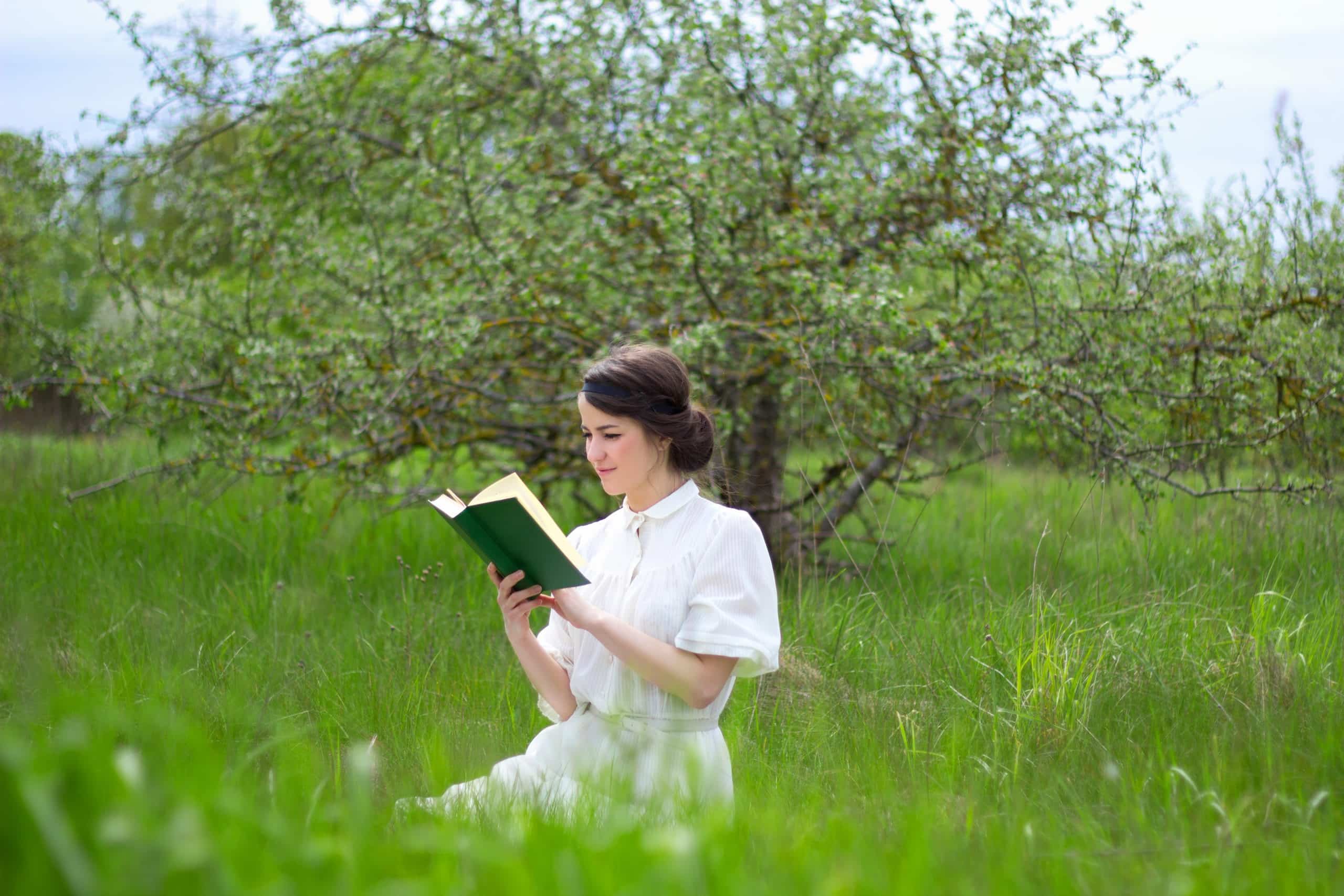 Beautiful woman sitting with book on summer meadow.