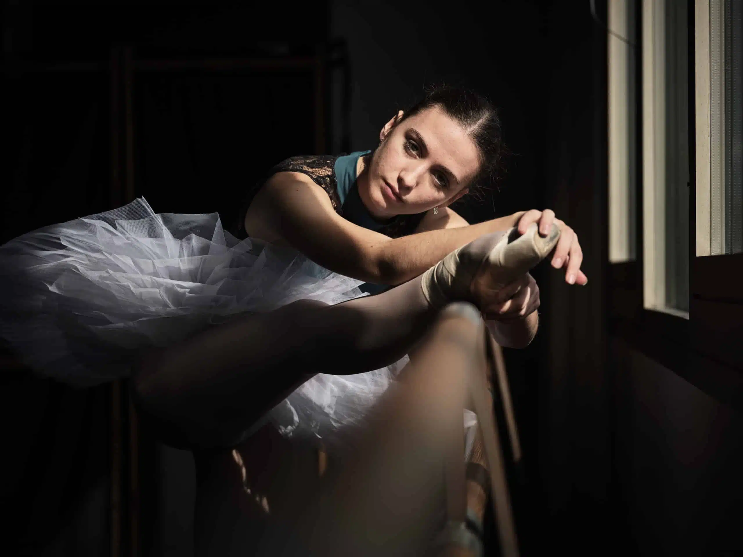 Young ballerina stretching leg on barre.
